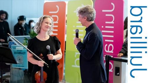 man holding a microphone speaking to a woman holding a violin